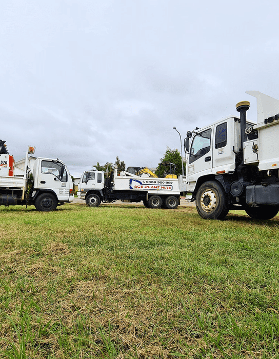 Three white utility trucks parked on grass under cloudy skies, ready for earthmoving Brisbane or plant hire Brisbane projects.